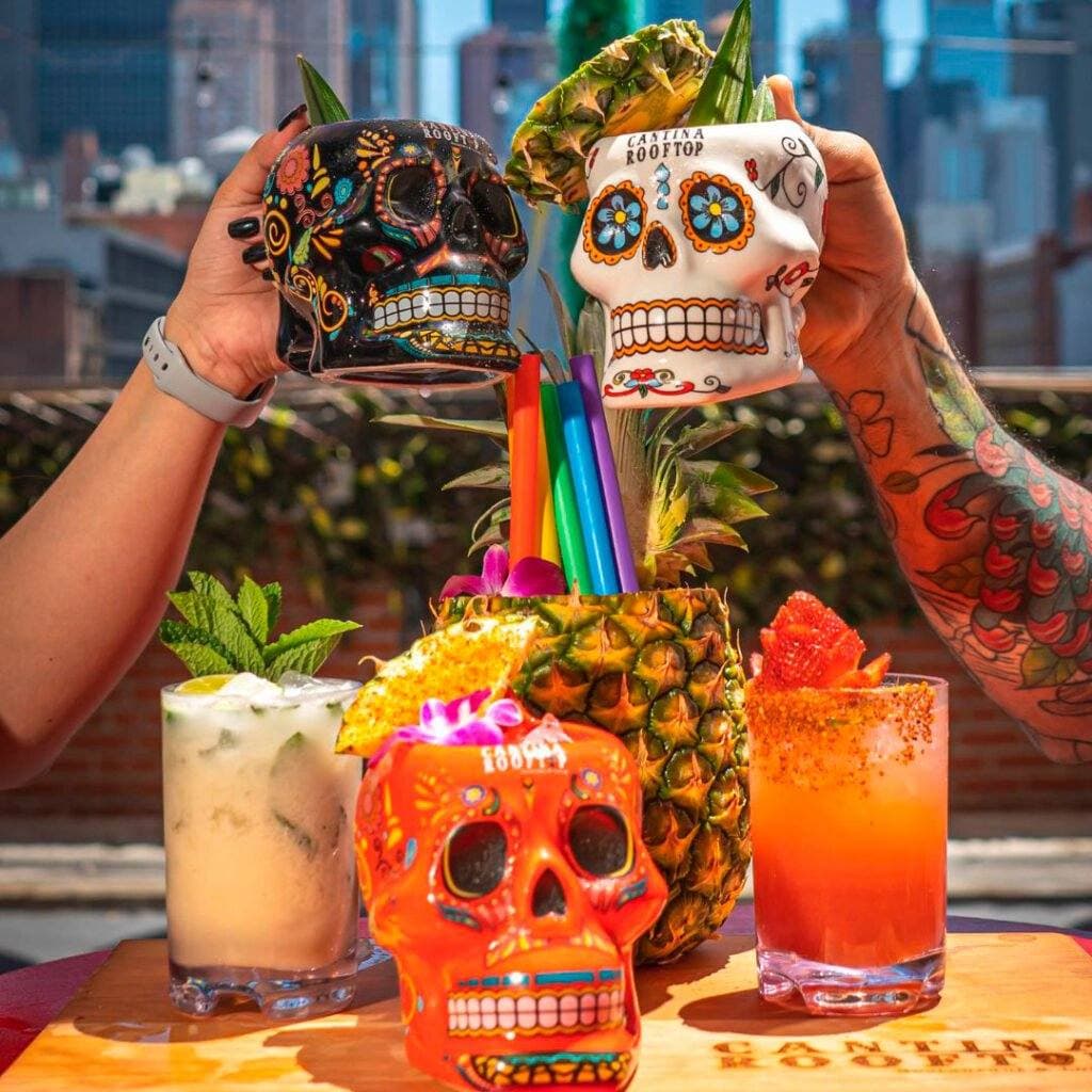 Skull mug margarita and a pineapple cocktail held up against the skyline