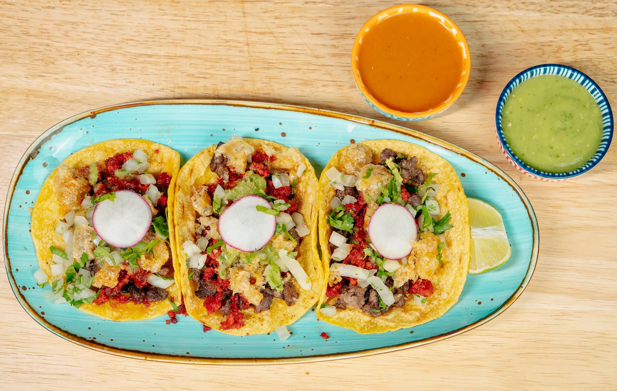 Three tacos on a blue plate with two salsas