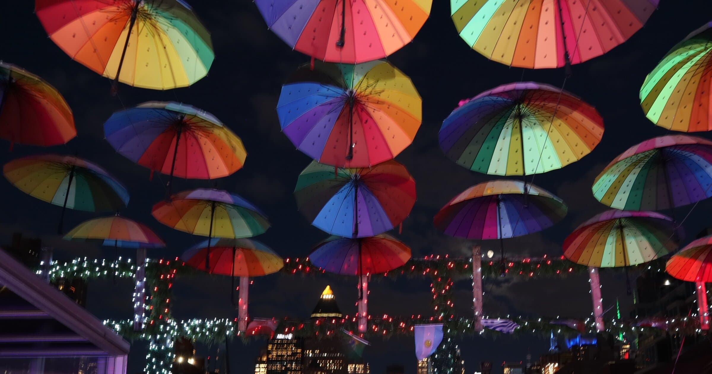 Rainbow umbrellas lit up over the rooftop at night