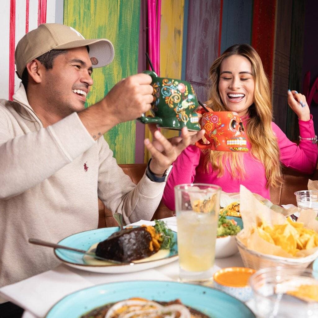 Two guests laughing over drinks and tacos
