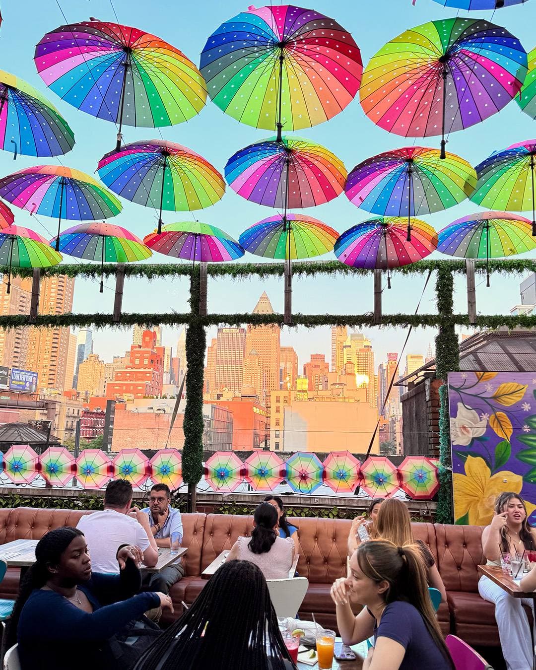 Diners on the rooftop at sunset under rainbow umbrellas