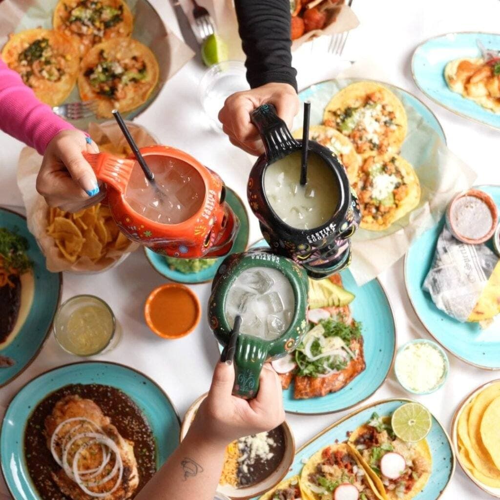 Hands reaching across a table of tacos, guacamole and margaritas