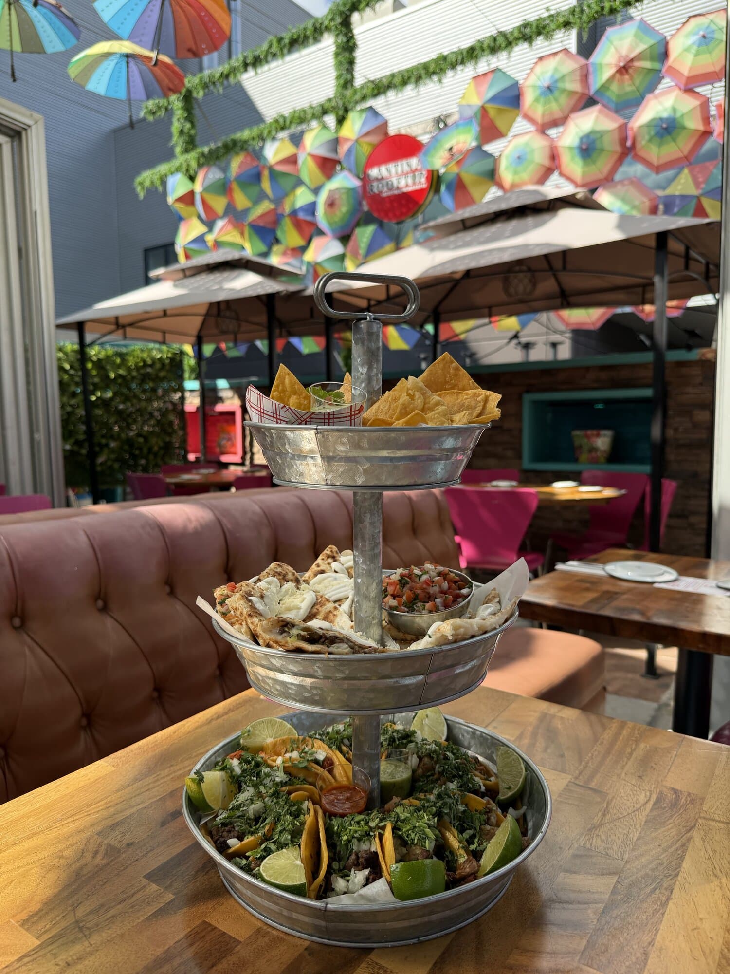 A three-tier Taco Tower with tortilla chips, quesadillas and tacos on a table under the rainbow umbrellas