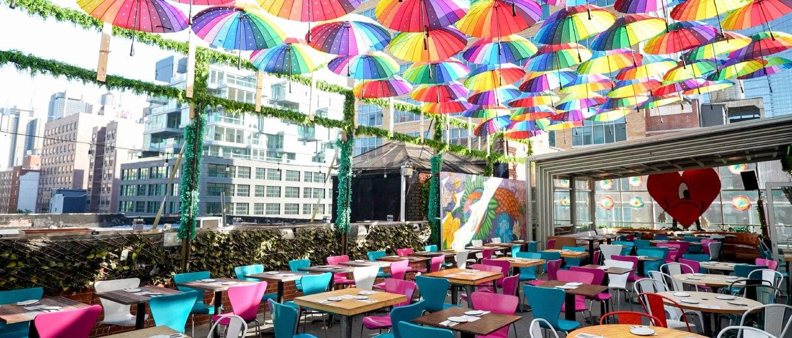 The rooftop with the glass roof open: rainbow umbrellas overhead and glass walls along the dining room